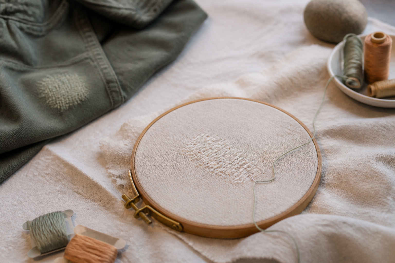 Tambour à broder en bois posé sur une toile écrue, entouré d'écheveaux de fils colorés et d'une paire de petits ciseaux