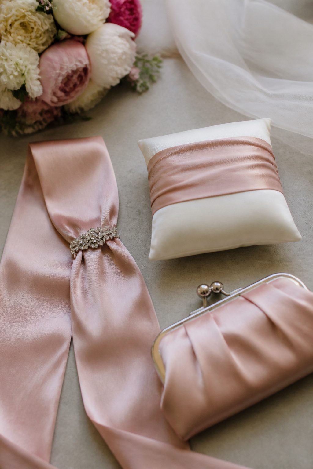 Sur une table de fleuriste en bois clair, près d'une fenêtre, un corsage de roses blanches et de feuillage posé à plat, à côté d'un aimant rond, d'une épingle à tête nacrée et d'une aiguille enfilée de fil blanc, lumière douce de fin de matinée, cadrage serré à hauteur de table.