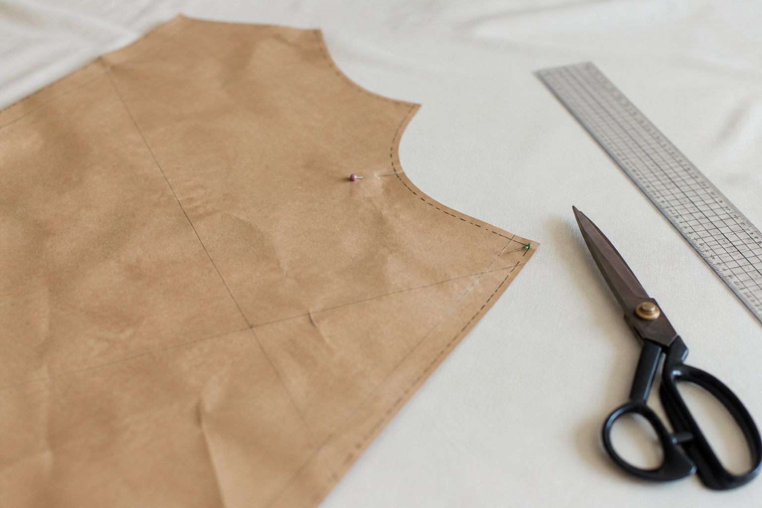 Pièce de patron en papier kraft épinglée sur un coton uni, une règle de tailleur et une paire de ciseaux posées à côté